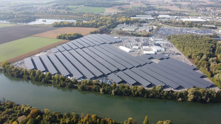 Vue aérienne d'un vaste parking couvert d'ombrières photovoltaïques en bord de rivière, Oise